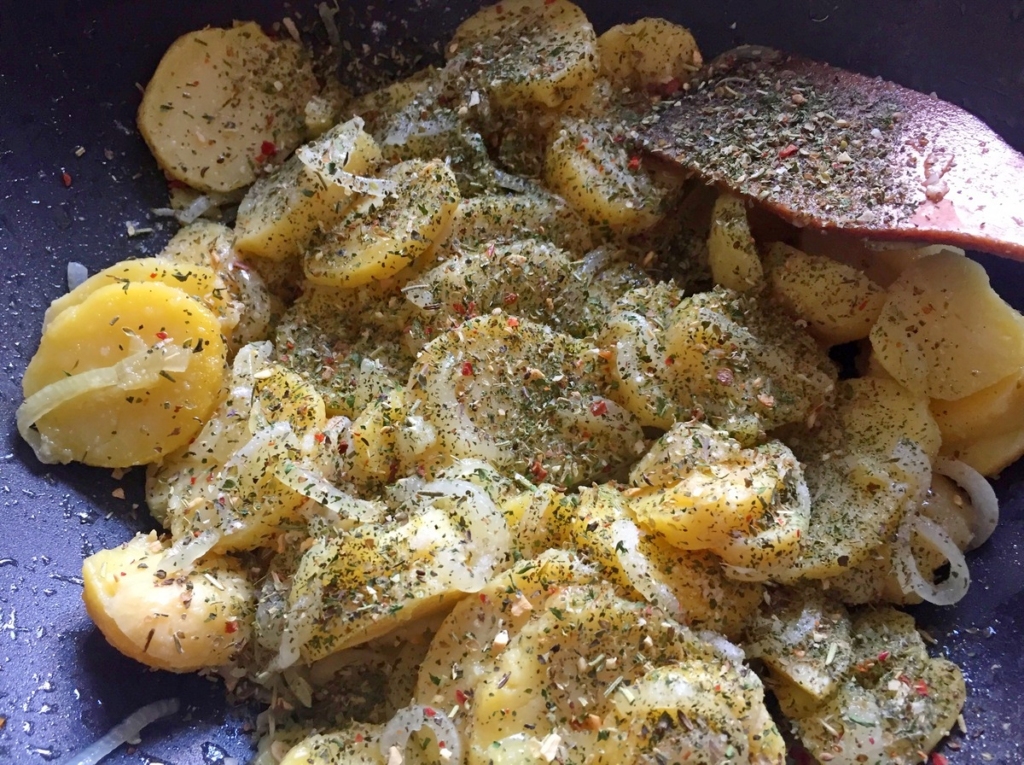 Нарізану кружальцями варену картоплю відправляємо на сковорідку до цибулі. Додаємо сіль, перець, подрібнену дольку часнику, трави